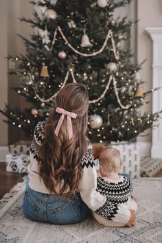 a mother and her baby sitting in front of a christmas tree