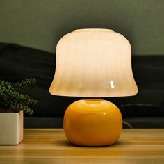 a yellow lamp sitting on top of a wooden table next to a potted plant