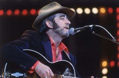 a man wearing a cowboy hat and holding a guitar in front of a microphone on stage