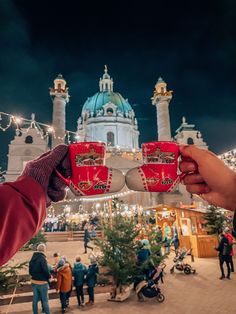 two people holding red cups in front of a building with christmas lights on the roof