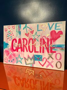 a painting that says i love caroline on top of a glass table in front of a blue wall