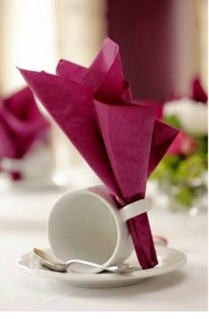 an origami flower is placed in a white plate on a table with pink napkins