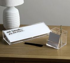 a desk with a pen, business card holder and lamp