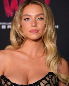 a woman with long blonde hair wearing a black dress and posing for the camera at an event