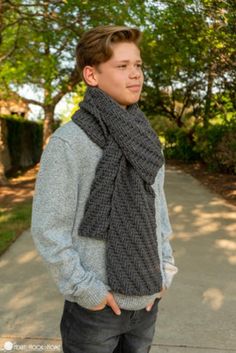 a young man is standing on the sidewalk wearing a gray sweater and black knitted scarf