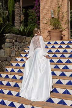 a woman is standing on some steps wearing a white wedding dress with long sleeves and an open back