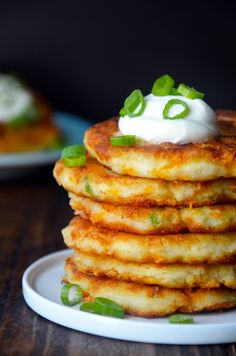 a stack of pancakes topped with sour cream and green onions on a white plate sitting on a wooden table