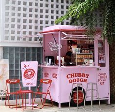 a pink ice cream cart sitting on the side of a road next to two red chairs