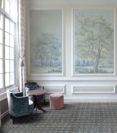 an empty room with two chairs and paintings on the wall behind them, in front of a window