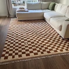 a white couch sitting on top of a wooden floor next to a large rug covered in brown and white squares