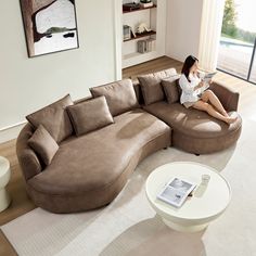 a woman sitting on top of a brown couch in a living room next to a window