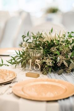 the table is set with plates and place settings for guests to sit at, along with greenery