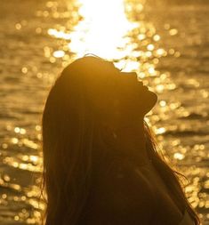 a woman standing in front of the ocean at sunset with her eyes closed and sun shining behind her