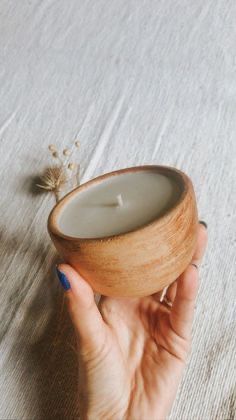 a person holding a small wooden bowl with a candle in it's middle and a flower on the other side