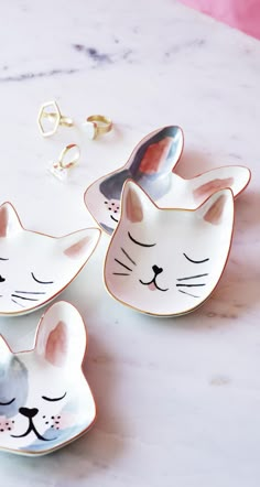 three cat shaped dishes sitting on top of a white marble counter next to each other