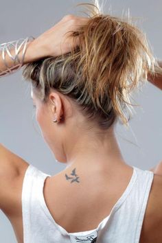 a woman with a tattoo on her back is holding her hair in the air and looking at something behind her