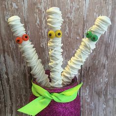 some white straws with googly eyes and green ribbon on them in a purple vase