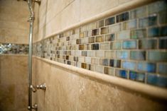 a tiled wall in a bathroom next to a shower with glass tiles on the walls