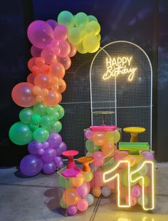 an arch made out of balloons with the number 11 on it and a neon sign that says happy birthday