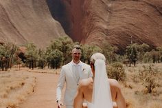 a bride and groom standing in front of a rock formation at the base of a mountain