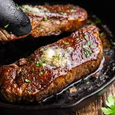 two steaks being cooked in a skillet with sauce and parsley on the side