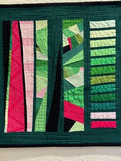 a green and pink quilted wall hanging on a wall next to a white wall