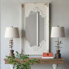 a white mirror sitting on top of a wooden mantle next to a plant and two lamps