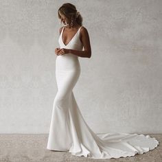 a woman in a white wedding dress standing against a wall with her back turned to the camera