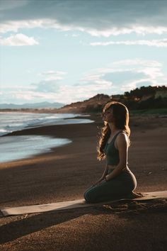 a woman sitting on top of a wooden plank next to the ocean with her eyes closed