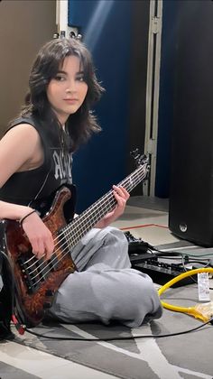 a woman sitting on the floor with a guitar in her hand and headphones around her neck