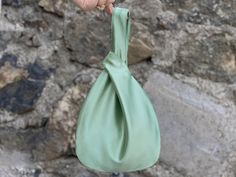 a hand holding a green bag in front of a stone wall