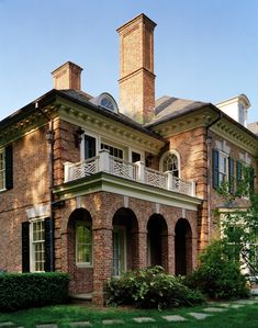 an old brick house with two chimneys and balconies on the second story, surrounded by green grass