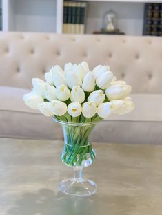 a glass vase filled with white tulips sitting on a table next to a couch