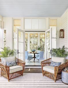 the front porch is decorated with wicker furniture and potted plants on either side