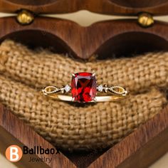 a red stone ring sitting on top of a heart shaped wooden box with two diamonds around it