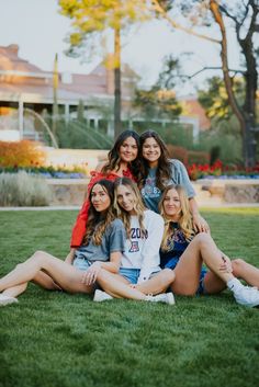 a group of young women sitting on top of a lush green field next to each other