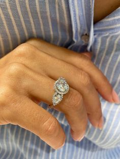 a woman's hand wearing a ring with two diamonds on it and a blue striped shirt