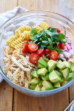 a glass bowl filled with pasta salad on top of a wooden table