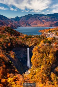 an aerial view of a waterfall surrounded by mountains and trees in fall colors, with the town below