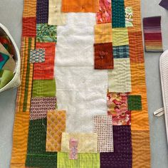 a quilted table runner with various colored squares on it and a pair of scissors next to it