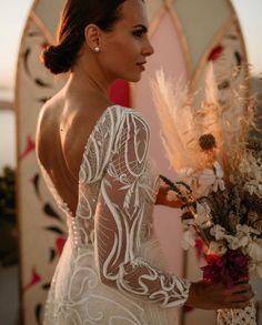 a woman in a wedding dress holding flowers and looking at the back of her dress