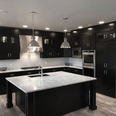 a large kitchen with black cabinets and white marble counter tops