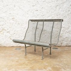 a metal bench sitting in front of a white wall