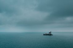 a large boat floating on top of the ocean under a cloudy sky with a lighthouse