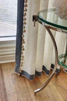 a glass table sitting next to a window with drapes on the windowsills