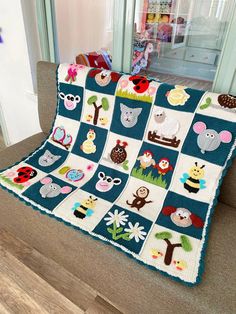 a crocheted blanket with animals and trees on it sitting on a couch in front of a window