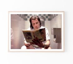 a man reading a book while sitting on the floor in a bathroom with tiled walls