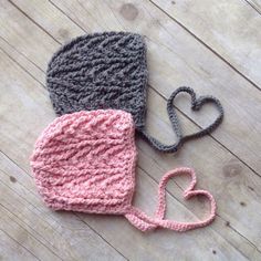 two crocheted hats are laying on the floor next to each other, one with a heart