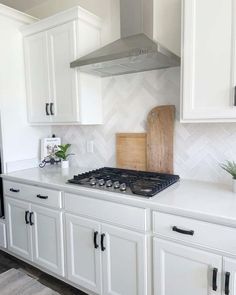 a kitchen with white cabinets and stainless steel range top hood over the stove, surrounded by potted plants