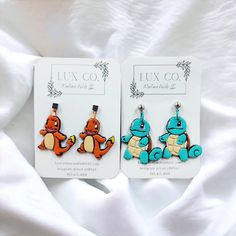 two earrings with cartoon characters on them sitting on a white bed sheet in front of a card